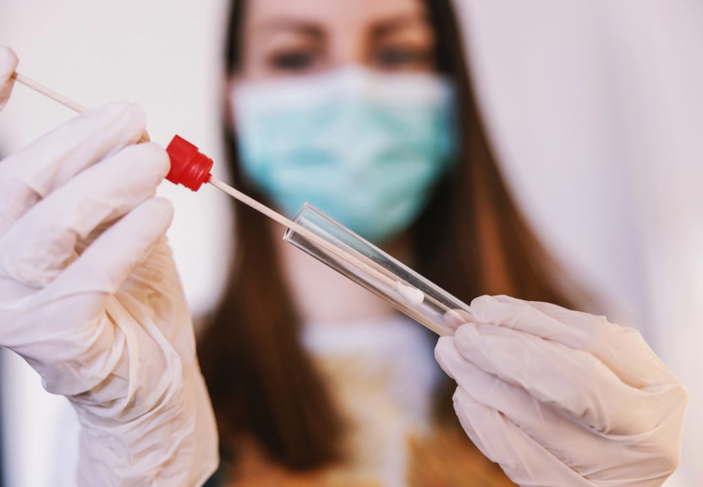 Masked clinician handles sterile swab and test tube for sample collection; accurate screening at best std testing houston.