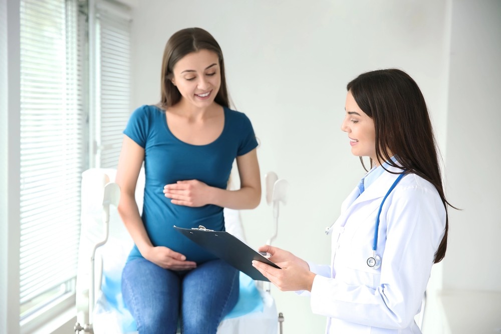 Pregnant woman on exam table with doctor holding a clipboard. They might discuss important prenatal labs like cheap sti testing Houston.