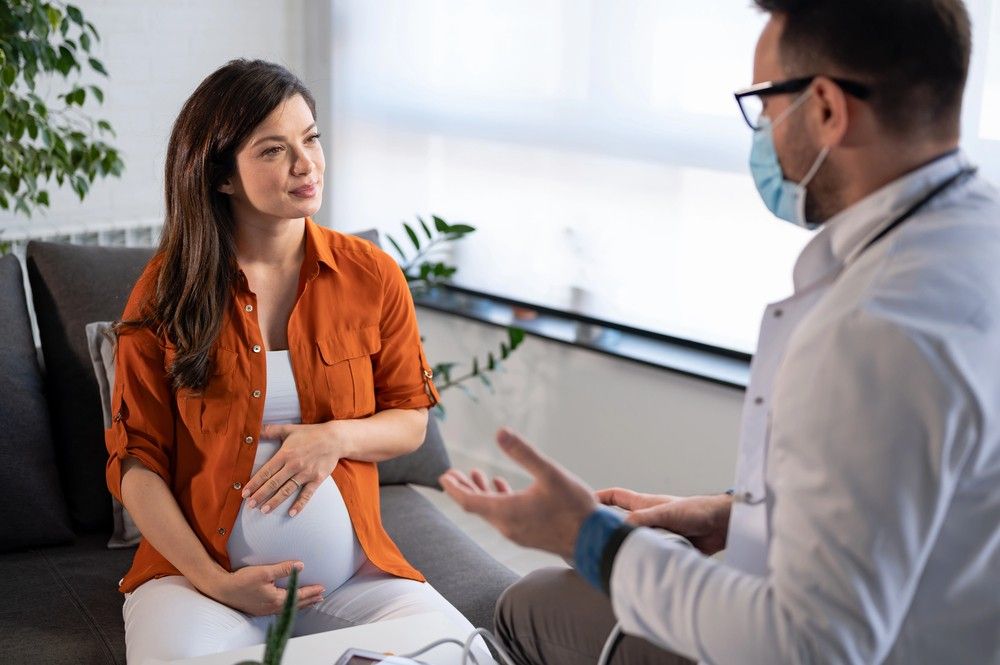 Pregnant woman talks with masked doctor on couch. A consultation is key for screenings like cheap sti testing Houston.
